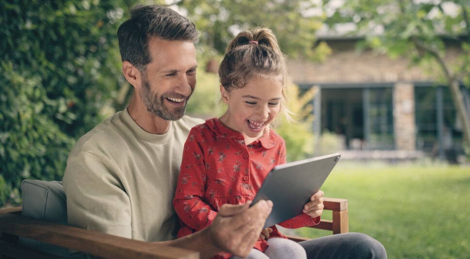 Ein Vater schaut mit seiner Tochter gemeinsam etwas auf dem Tablet und freut sich über das Angebot 1 Jahr GigaTV geschenkt