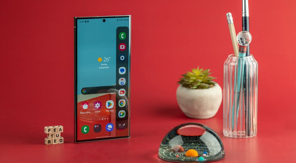 Großes Smartphone stehend neben bunter Glaskugel und Kaktus auf rotem Untergrund