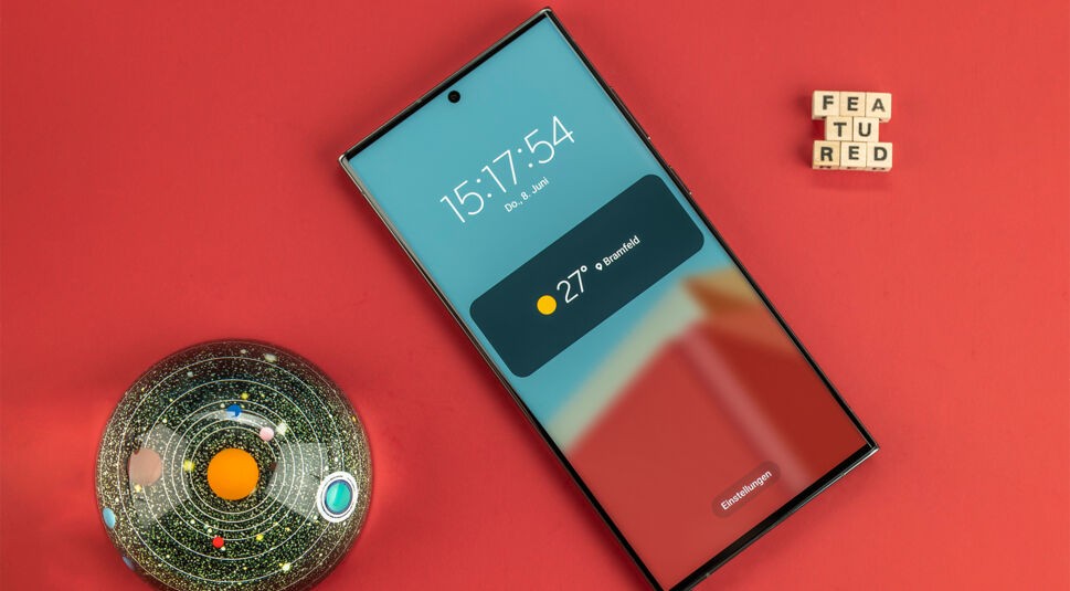 Das große Display des Galaxy S23 Ultra auf rotem Untergrund, daneben eine Glaskugel und Buchstabenwürfel.