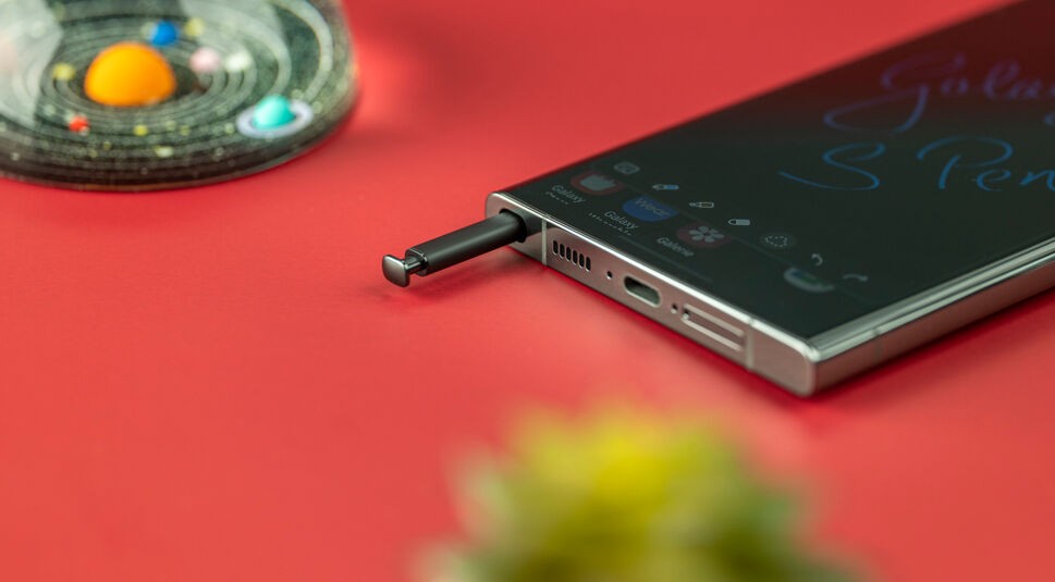 Unterer Rand eines Smartphones, aus dem ein Eingabestift herausragt auf roter Fläche