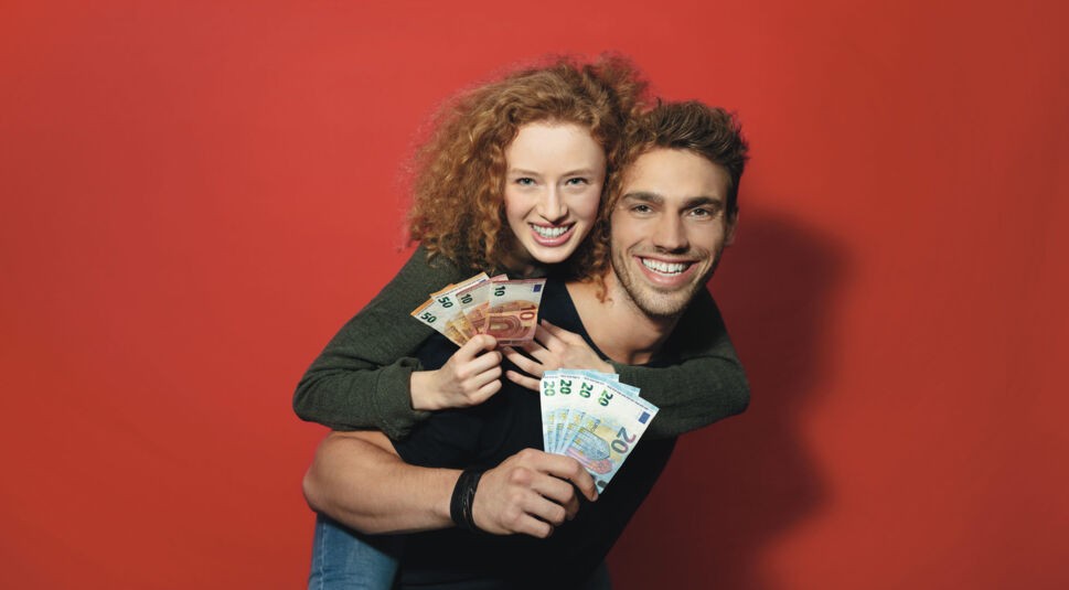 Zwei Personen posieren vor einem roten Hintergrund und freuen sich über das Freund:innen werben Programm von Vodafone