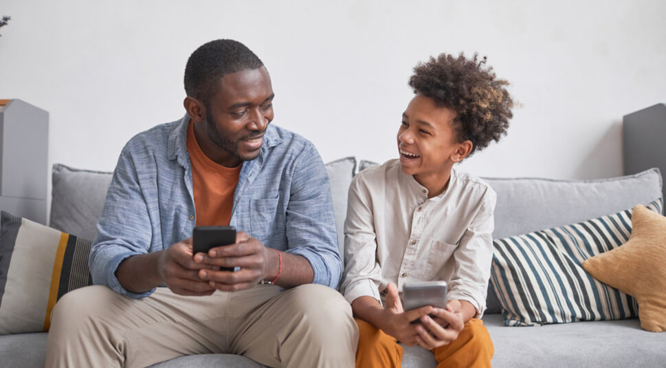 Auf dem Bild in dem Artikel zu den Kindertarifen von Vodafone sitzen ein Mann und ein Junge lachend auf einem Sofa.