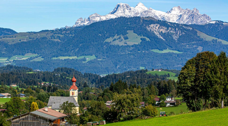 Ein kleiner Ort mit Pfarrkirche vor einem Bergpanorama