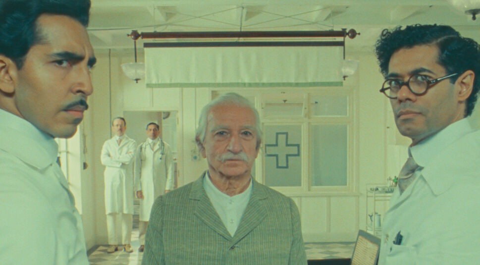 Zwei Ärzte stehen mit skeptischem Blick links und rechts von einem alten Mann mit grauen Haaren und Schnauzer.