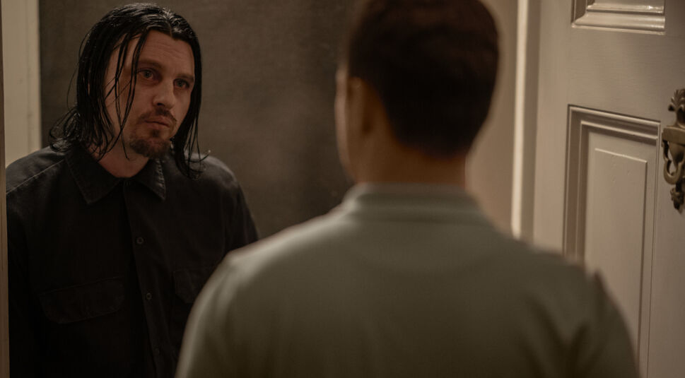 Ein Mann mit schulterlangen schwarzen Haaren und Bart blickt einen anderen Mann mit kurzen Haaren fragend an. 