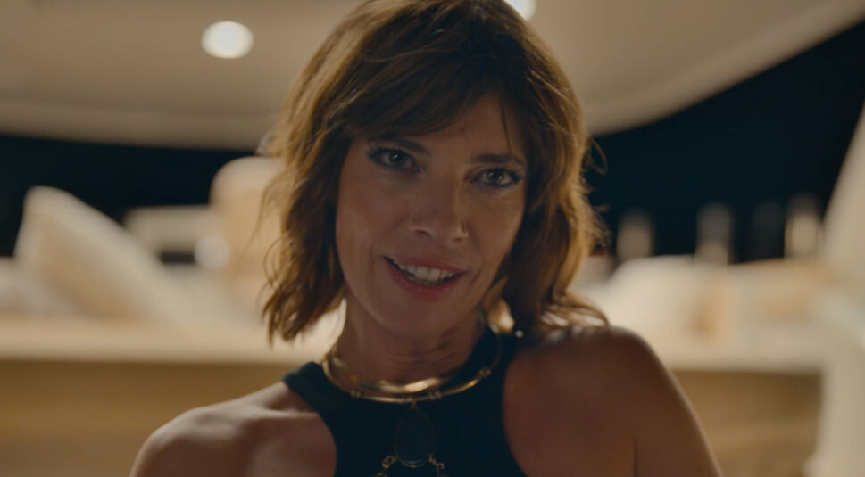Ein Szenenfoto aus dem Netflix-Film „Tödliche Einladung“ zeigt Schauspielerin Maribel Verdú mit dunklen, schulterlangen Haaren und einem listigen Grinsen.
