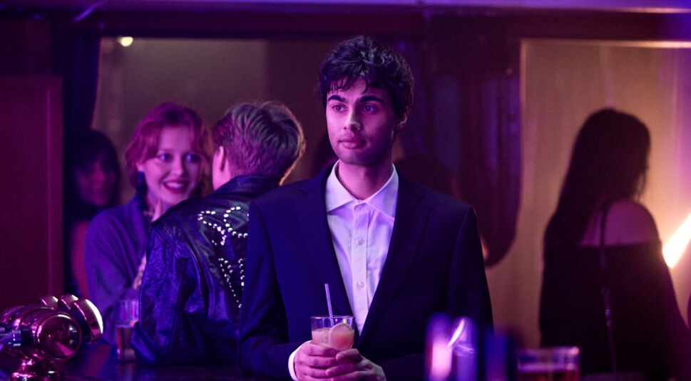 William Spetz in Tore: Ein Junger Mann im Anzug steht mit einem Cocktail in der Hand an einer belebten Bar.