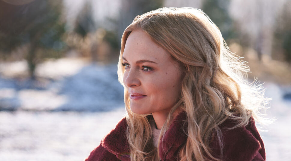 Last. Christmas. Ever! bei Netflix: Eine Frau mit blonden langen Haaren steht lächelnd mit einem weinroten Wintermantel in einer verschneiten Landschaft. 