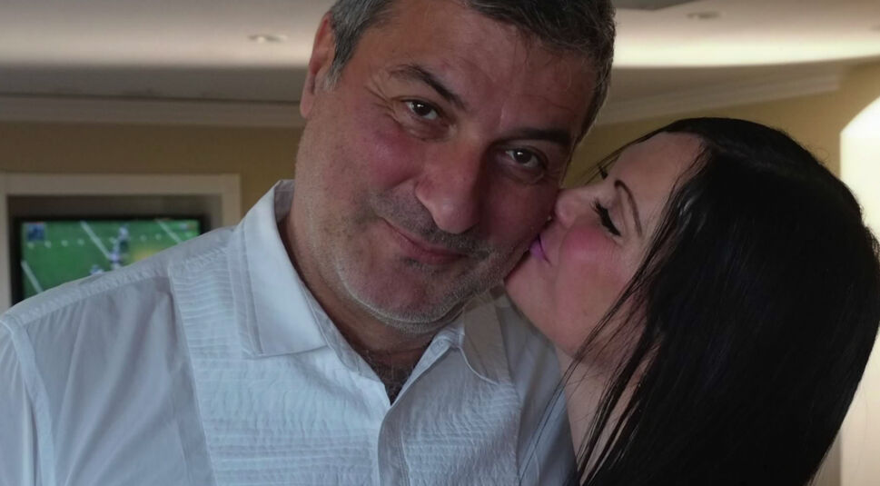 Bad Surgeon - Liebe unter dem Messer: Ein Mann mittleren Alters in einem weißen Hemd senkt den Kopf und grinst, während ihm eine Frau mit schwarzen Haaren einen Kuss auf die Wange drückt.