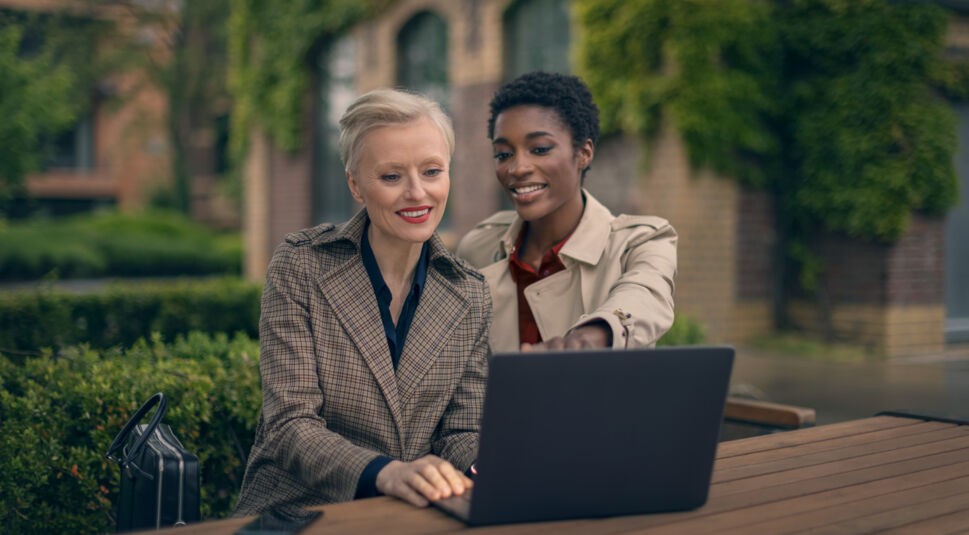 Zwei Frauen schauen auf einen Laptopbildschirm und stehen im Grünen.