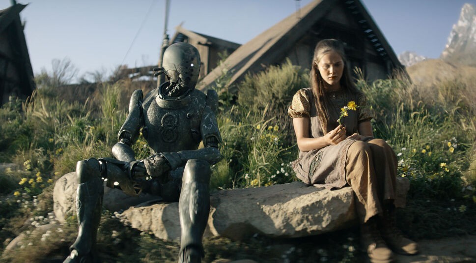 Ein Android und eine junge Frau sitzen gemeinsam auf einem Stein,