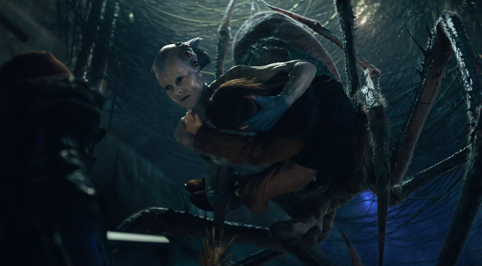 Jena Malone als Spinnenfrau Harmada. Sie hat eine Person in ihren Fängen