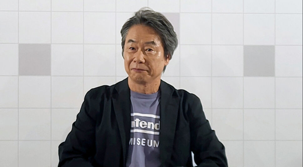 Auf dem Bild zum Zelda Live-Action-Film ist Shigeru Miyamoto, der legendäre Spieleentwickler und Schöpfer von „The Legend of Zelda“, zu sehen. Er trägt ein schwarzes Sakko über einem T-Shirt mit der Aufschrift „Nintendo Museum“. Der Hintergrund zeigt eine hell gekachelte Wand. Miyamoto blickt ruhig und selbstbewusst in die Kamera.