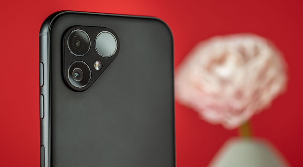 Die Rückseite des Fairphone 5 mit Kamera, im Hintergrund eine Blumenvase vor rotem Hintergrund