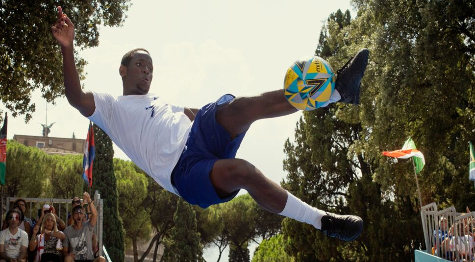 Vinny (Micheal Ward) in Fußballkleidung, während er einen Fußball mit dem Fuß kickt.
