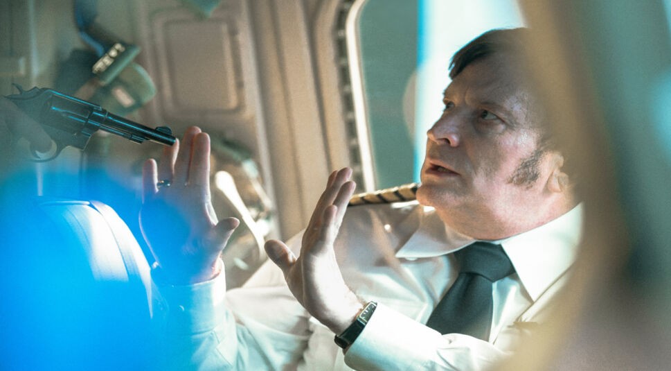 Szenenbild aus der Serie Die Entführung des Flugs 601: Ein Pilot wird mit einer Waffe bedroht.