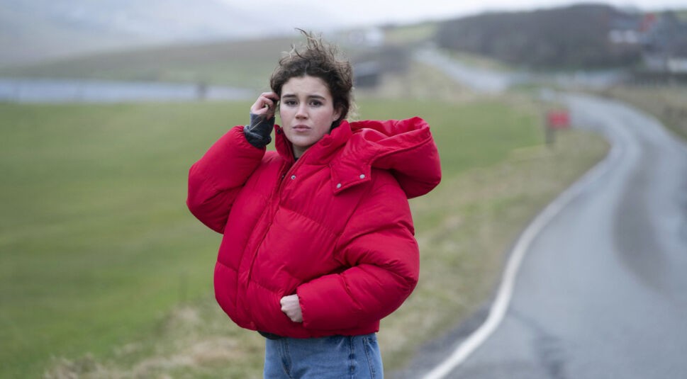 Eine junge Frau steht auf einer Landstraße und telefoniert mit dem Handy.