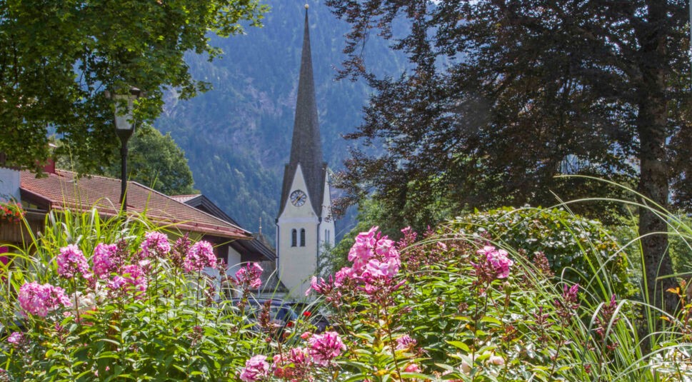 Die Kirche von Bayrischzell, im Vordergrund Büsche und rosafarbene Blumen