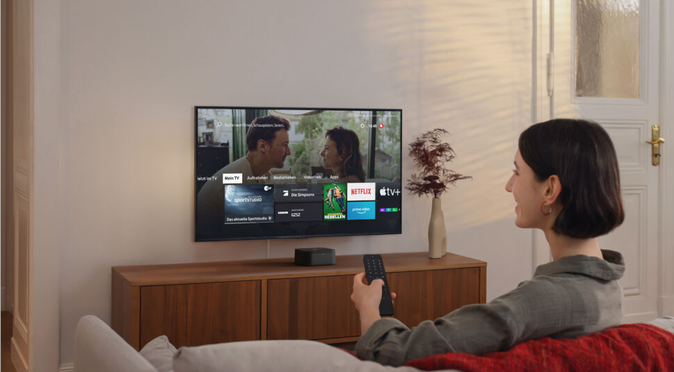 Eine Frau sitzt auf der Couch vor dem TV und nutzt die Fernbedienung der GigaTV Home Sound