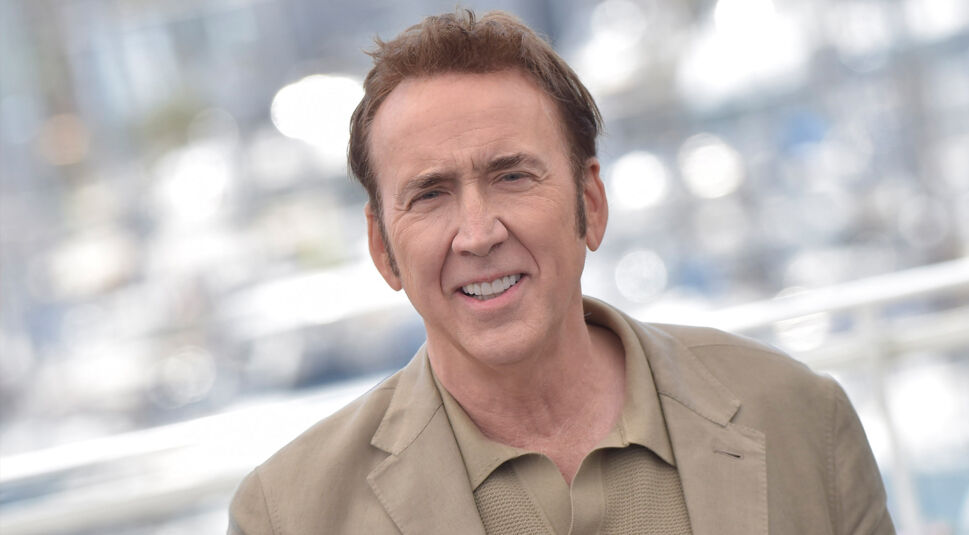 Auf dem Bild in dem Artikel zur Serie Spider-Noir ist Nicolas Cage zu sehen. Er guckt in die Kamera und hat ein leichtes Lächeln aufgesetzt. Er trägt ein beiges Poloshirt und einen beigen Blazer.