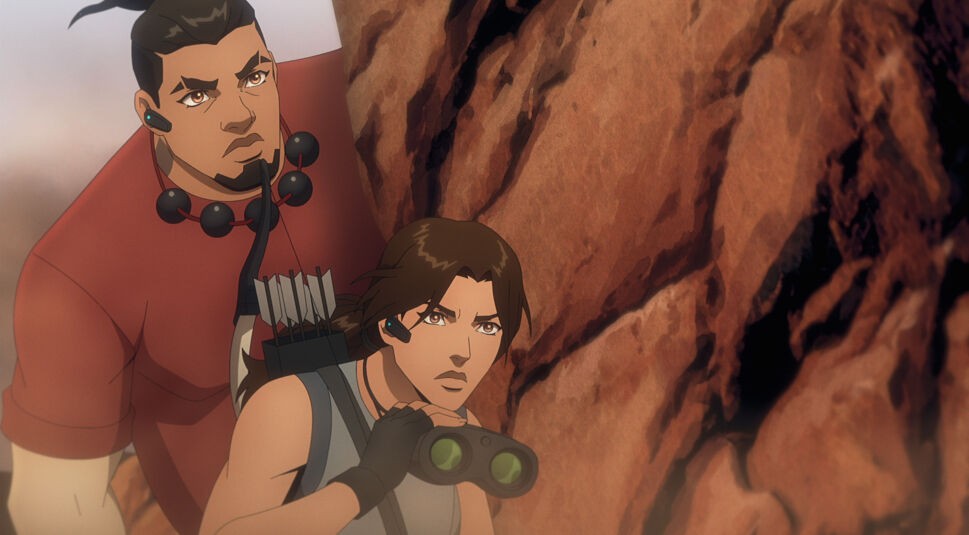 Auf dem Bild aus Tomb Raider: The Legend of Lara Croft sind die Charaktere Lara Croft und Jonah Maiava zu sehen. Lara, mit entschlossenem Blick und Fernglas in der Hand, trägt ein graues Top und Handschuhe. Jonah steht hinter ihr und blickt konzentriert über ihre Schulter. Beide befinden sich an einem Felsen, was eine angespannt-abenteuerliche Atmosphäre vermittelt.