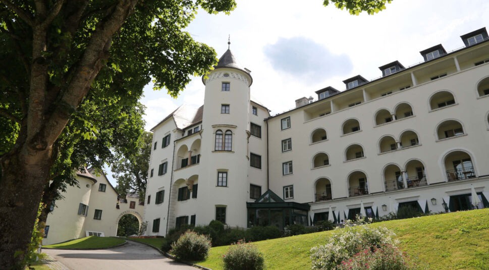 Ein edles, weißes Hotel mit Turmspitze in grüner Landschaft