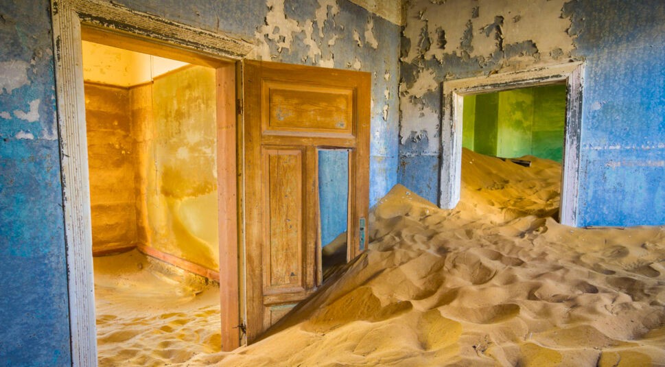 Blick in die Zimmer eines verlassenen Hauses, in dem sich Wüstensand auftürmt