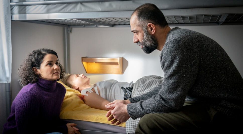 Schauspielerin Nagmeh Alaei (links) hockt vor einem Bett und unterhält sich mit einem Mann.