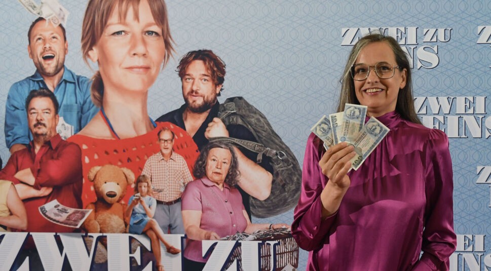 Regisseurin Natja Brunckhorst stehjt mit einem Bündel Geldscheine in der Hand vor einem Filmplakat von Zwei zu eins