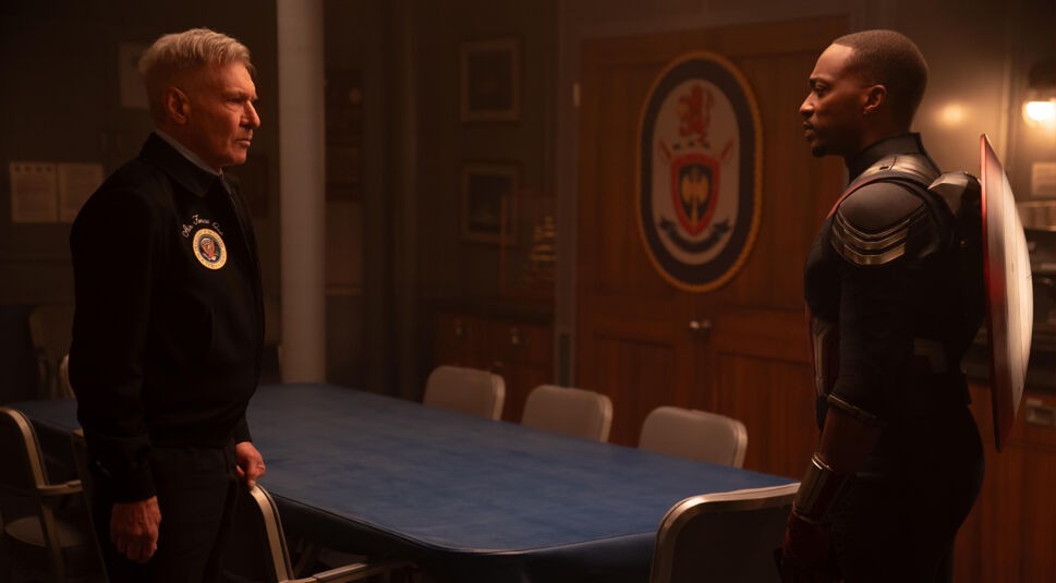 Auf dem Bild im Artikel zu Captain America 4: Brave New World sind zwei Personen zu erkennen. Sie stehen sich mit etwa einem Meter Abstand gegenüber in einem schwach beleuchteten Konferenzraum. Links steht der Präsident der USA (gespielt von Harrison Ford). Er blickt sein Gegenüber, das am rechten Bildrand steht, ernst an. Die Person am rechten Bildrand ist Captain America. Auch er blickt den Präsidenten ernst an. Er trägt seine Uniform und sein Schild auf dem Rücken.