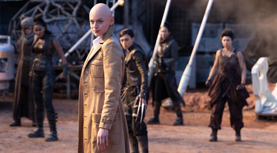 Auf dem Bild aus Deadpool & Wolverine ist Emma Corrin als Cassandra Nova zu sehen. Cassandra Nova steht entschlossen im Vordergrund, während vier weitere Charaktere im Hintergrund kampfbereit wirken. Die Szene ist angespannt und dynamisch.