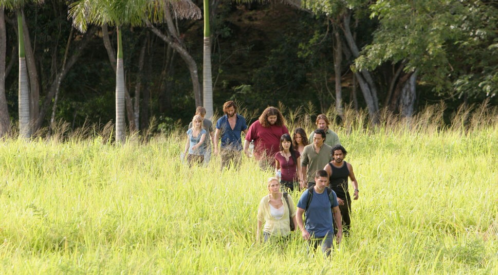 EIne Gruppe der Überlebenden in der Fernsehserie Lost wandern durch hohes Gras. Sie gehen auf die Kamera zu. Sie scheinen gerade aus dem Dschungel zu kommen, der den Horizont im Hintergrund verdeckt. Ganz vorne geht Dr. Jack Shepard (gespielt von Matthew Fox) und führt die Gruppe an.