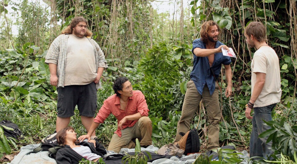 In der Serie Lost hockt Jin-Soo Kwon im Dschungel neben einer verletzten Person, die auf dem Boden liegt. Drei weitere Überlebende des Flugzeugabsturzes in den er geraten ist, stehen um ihn herum und scheinen zu diskutieren. Einer von ihnen zeigt einem anderen einen Gegenstand und erklärt ihm etwas dazu. Jin-Soo Kwan schaut zu ihnen hoch.