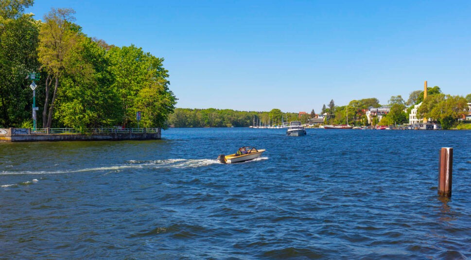 Blick auf einen See im Grünen, auf dem ein Motorboot fährt