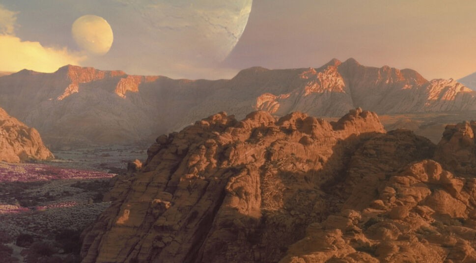 Im Bild zur Borderlands-Filmkritik ist die Landschaft des Planeten Pandora zu sehen, auf dem sich die Handlung des Films abspielt. Zu sehen sind felsige bräunliche Berge, die von Sonnenlicht angestrahlt werden. Links ist ein Stück des dazwischenliegenden Tals zu erkennen . Hier wachsen lila Bodenpflanzen. Oben links sind zwei voreinanderliegende Planeten im Himmel zu erkennen, sowie eine helle Wolke.
