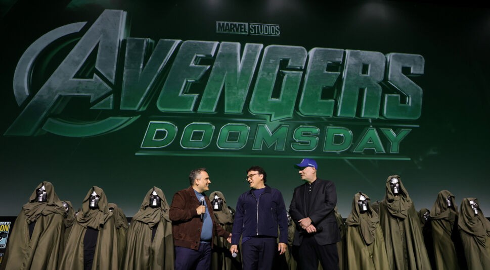 Bei der San Diego Comic Con 2024 wird der Titel „Avengers: Doomsday“ vor einem großen Publikum präsentiert. Auf der Bühne stehen mehrere Personen in Doctor-Doom-Kostümen mit grünen Umhängen und silbernen Masken, während im Hintergrund ein großes Logo des Films „Avengers: Doomsday“ von Marvel Studios zu sehen ist.