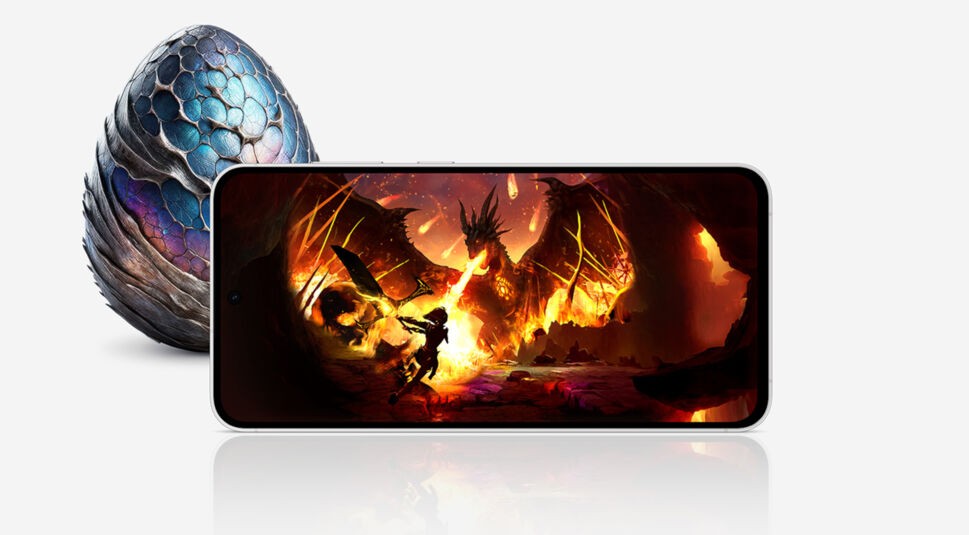Das Smartphone Galaxy S24 FE mit einem Drachen auf dem Display, hinter dem Gerät vor hellem Hintergrund ein blaues Fantasy-Ei.