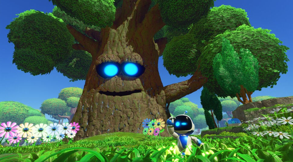 Auf dem Bild aus Astro Bot Test ist der kleine Roboter Astro Bot zu sehen, wie er in einer grünen, farbenfrohen Umgebung steht. Links hinter ihm ragt ein großer, freundlicher Baum mit leuchtend blauen Augen empor, der ihn ansieht. Im Vordergrund wachsen bunte Blumen, und die Landschaft ist geprägt von sattem Gras und vielen Bäumen. Astro Bot schaut mit neugierigem Ausdruck in die Ferne, während die Sonne den klaren Himmel erhellt.