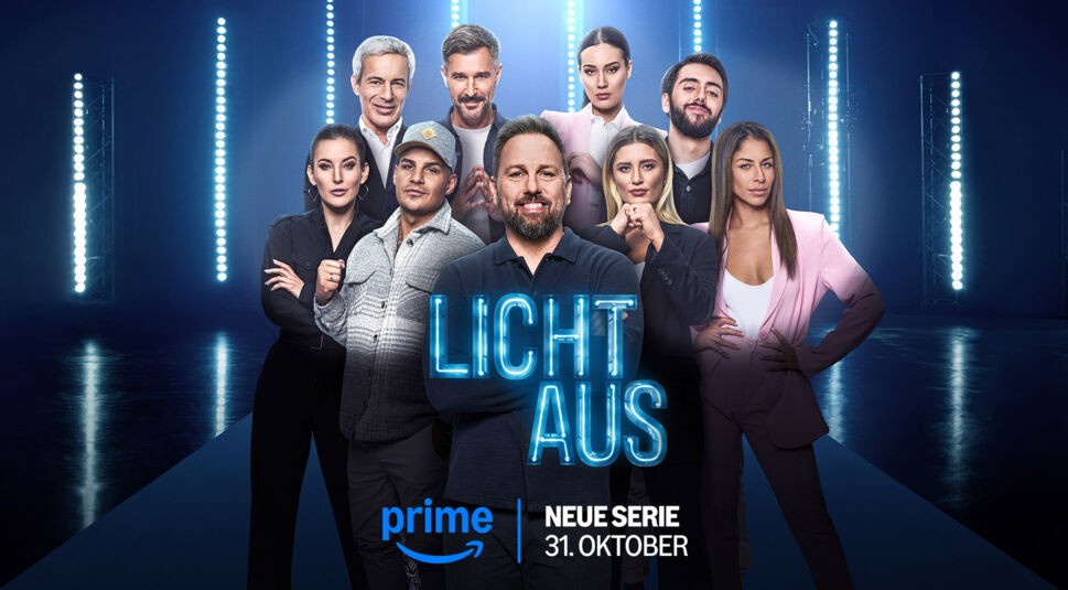 Auf dem Bild zur neuen Prime-Video-Show "Licht Aus" ist der gesamte Cast der Serie zu sehen. In der Mitte steht Moderator Steven Gätjen, umgeben von den Teilnehmern, darunter bekannte Gesichter wie Reality-TV-Stars und Prominente. Sie posieren in einer futuristisch beleuchteten Umgebung mit blauen und weißen Scheinwerfern im Hintergrund. Alle wirken entschlossen und bereit für die Show. Das Logo von "Licht Aus" und der Hinweis auf die Premiere am 31. Oktober sind prominent platziert.