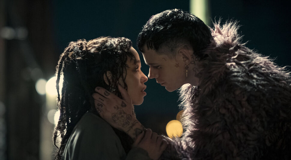 Auf dem Bild zu "The Crow Unterschiede" sind Bill Skarsgård (rechts) und FKA Twigs (links) in einer emotionalen und intensiven Szene zu sehen. Skarsgård, mit Tattoos im Gesicht und einer auffälligen Felljacke, hält FKA Twigs behutsam am Kopf, während sich ihre Stirnen fast berühren. Beide blicken sich tief in die Augen, was eine starke Verbindung und Intimität vermittelt. Die Szene ist stimmungsvoll beleuchtet, mit unscharfen Lichtpunkten im Hintergrund, die eine nächtliche Atmosphäre verstärken.