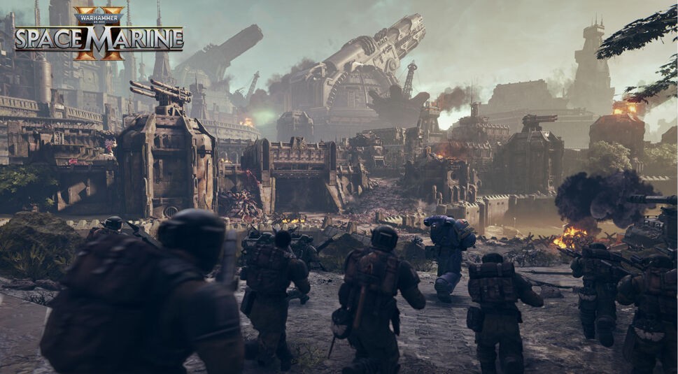 Auf dem Bild zu „Warhammer 40.000: Space Marine 2“ stürmen mehrere Soldaten, darunter ein blauer Space Marine, auf eine massive, befestigte Festung zu. Im Hintergrund sieht man gewaltige Geschütztürme und rauchende Trümmer, die eine intensive Schlacht andeuten. Der Himmel ist düster und von Rauchschwaden durchzogen, während Feuer und Zerstörung die Szene dominieren. Die Atmosphäre ist bedrohlich und hektisch, geprägt von einer epischen Kriegslandschaft im Universum von Warhammer 40.000.