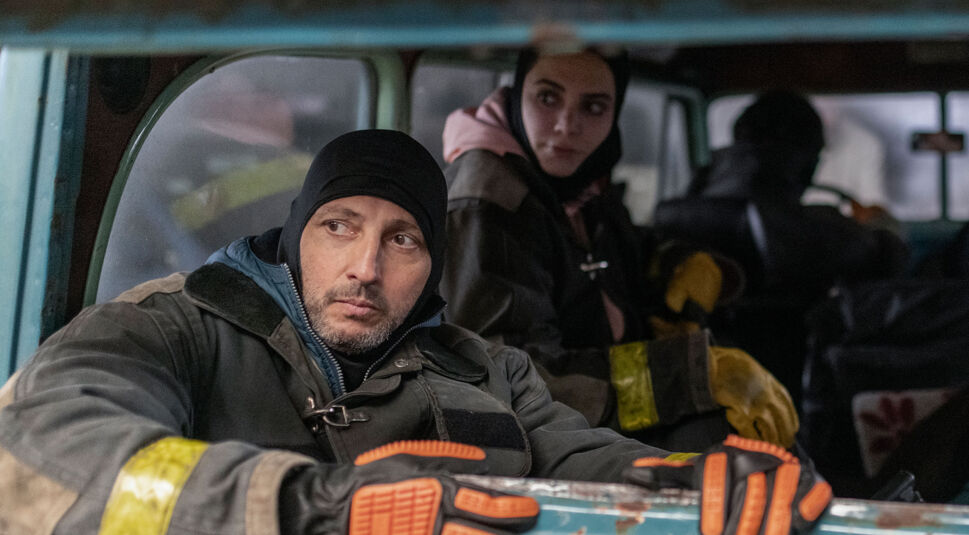 Auf dem Bild vom Eternauta-Netflix-Artikel ist der Cast der kommenden Netflix-Show Eternauta zu sehen. Im Vordergrund sitzt ein Mann in einem winterlichen, wetterfesten Outfit, mit einer schwarzen Mütze und auffälligen, orange-schwarzen Handschuhen. Sein Blick ist aufmerksam und ernst, als ob er nach etwas Ausschau hält. Im Hintergrund sind zwei weitere Personen zu erkennen, ebenfalls in dicker Outdoor-Kleidung. Sie sitzen in einem rustikalen Fahrzeug, das eine raue, dystopische Atmosphäre vermittelt. Die Szene lässt auf eine gefährliche Mission oder einen Überlebenskampf schließen, passend zur Handlung von Eternauta, die in einer apokalyptischen Welt spielt.