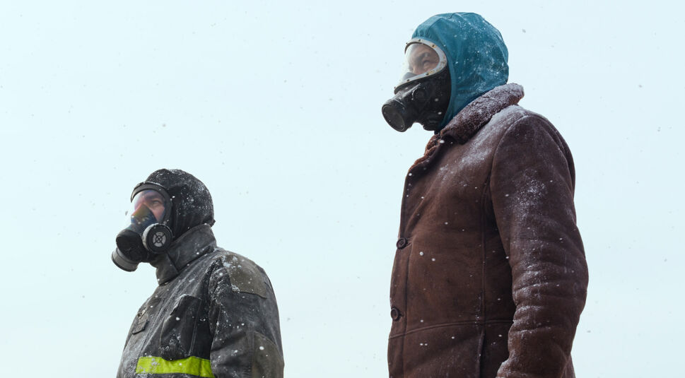 Auf dem Bild vom Eternauta-Netflix-Artikel sind zwei Charaktere aus der Netflix-Show Eternauta zu sehen. Beide Personen tragen dicke Winterkleidung und Gasmasken, während sie in eine schneebedeckte, trostlose Landschaft blicken. Die Kleidung wirkt robust und ist mit Schnee bedeckt, was auf extreme Witterungsbedingungen hinweist. Die Figuren stehen still und schauen in die Ferne, was eine bedrohliche, apokalyptische Stimmung erzeugt. Die Szene deutet auf die harschen Überlebensbedingungen hin, die typisch für die dystopische Welt von Eternauta sind, in der die Charaktere sich vor einer unbekannten Gefahr schützen müssen.