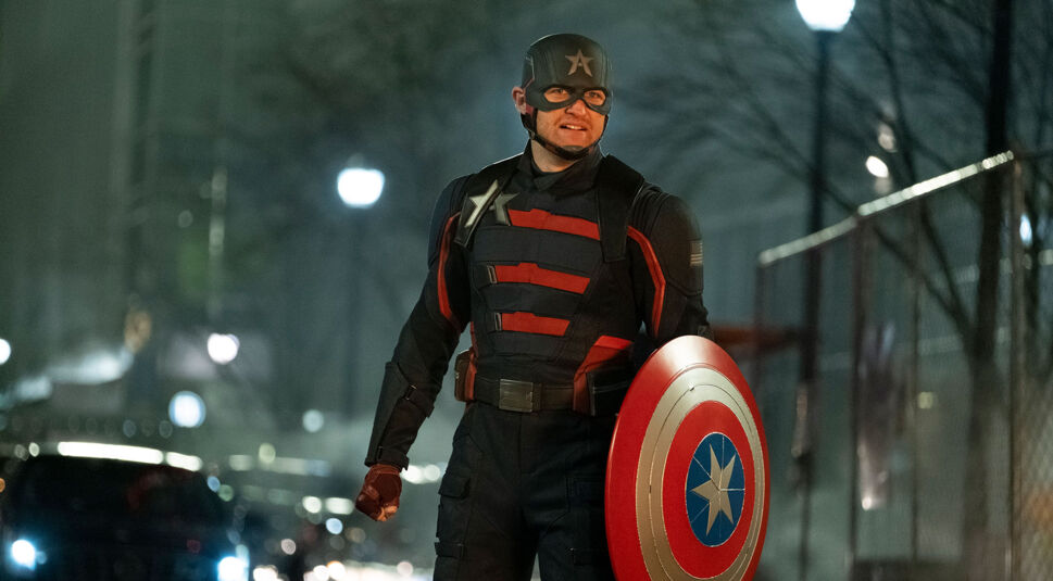 Auf dem Bild vom Thunderbolts-Team-Artikel ist John Walker, bekannt aus der Serie The Falcon and the Winter Soldier, zu sehen. Er trägt seine markante Uniform als Captain America-Nachfolger, mit einem dunklen Anzug und roten Streifen, und hält das ikonische Schild mit Sternmotiv in der Hand. Die Szene spielt nachts auf einer Straße, umgeben von Autos und leichtem Nebel, was eine düstere und angespannten Stimmung erzeugt. John Walker hat einen entschlossenen Gesichtsausdruck, bereit für die nächste Herausforderung.
