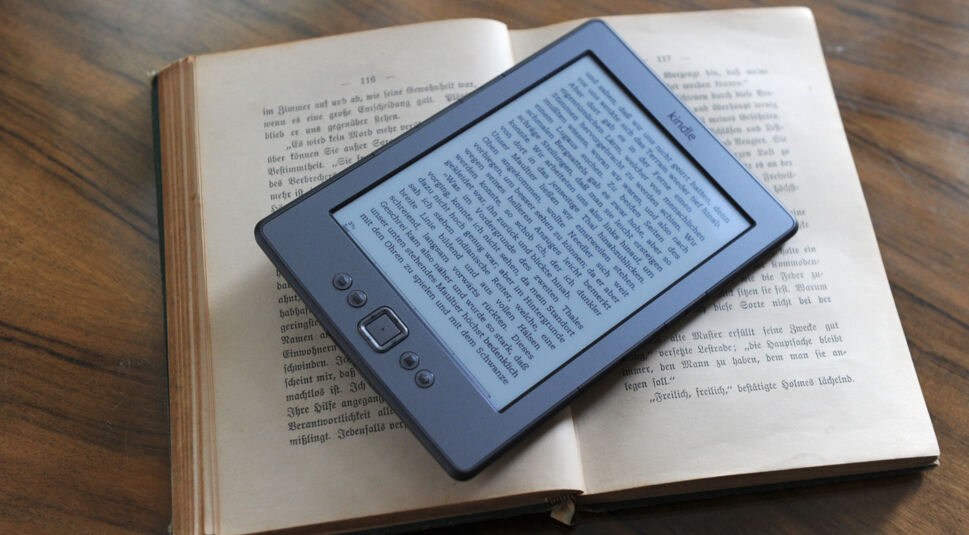 Ein Amazon Kindle eReader liegt auf einem aufgeschlagenem Buch.