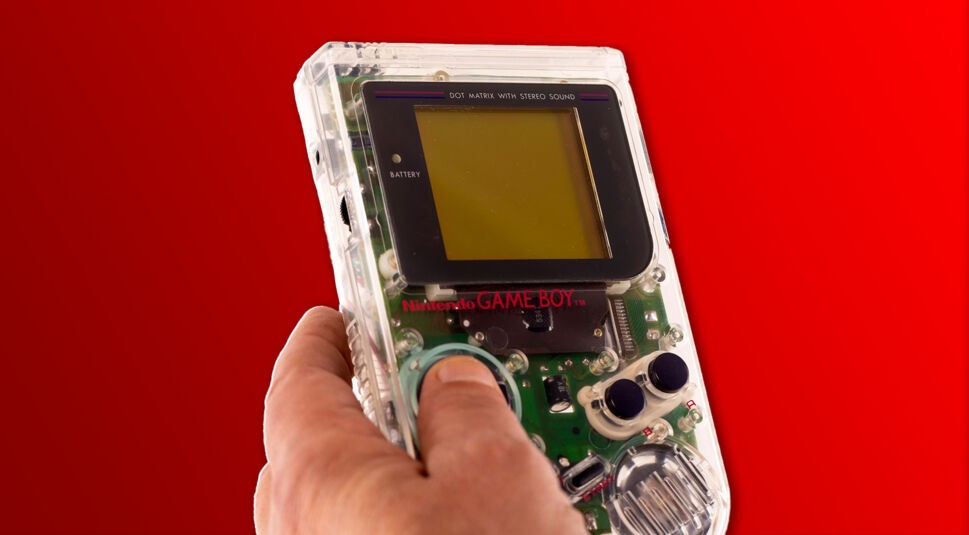 Ein Game Boy mit transparentem Gehäuse vor rotem Hintergrund