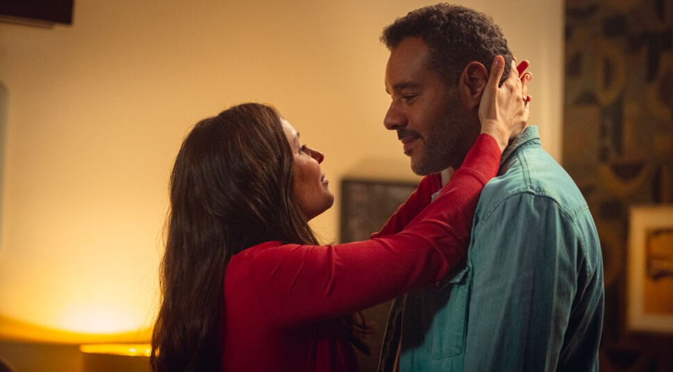 Auf dem Bild aus "Cassandra" sind Michael Klammer als David (rechts) und Mina Tander als Samira (links) in einer emotionalen Szene zu sehen. Samira trägt ein rotes Oberteil und hält David liebevoll am Kopf, während die beiden sich tief in die Augen sehen. Die warme Beleuchtung verstärkt die intime und romantische Atmosphäre.