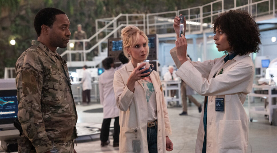 n dieser Szene aus Venom 3 stehen von links nach rechts Chiwetel Ejiofor in Militärkleidung, Juno Temple mit einem Kaffeebecher und Clark Backo, die ein Reagenzglas hält, in einem modernen Labor. Die Figuren wirken konzentriert und diskutieren offenbar eine wissenschaftliche Probe. Im Hintergrund sind weitere Wissenschaftler und Hightech-Geräte zu sehen, die die futuristische Atmosphäre unterstreichen.