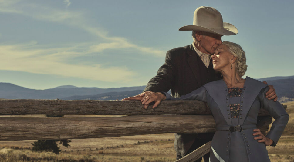 Auf dem Bild zur Yellowstone-Reihenfolge sind Jacob Dutton, gespielt von Harrison Ford, und Cara Dutton, dargestellt von Helen Mirren, in einer innigen Szene zu sehen. Vor der Kulisse der Weiten Montanas lehnt Jacob liebevoll an einem Holzzaun und küsst Cara zärtlich auf die Stirn. Die Szene strahlt Wärme, Vertrauen und tiefe Verbundenheit aus – typisch für die emotionale Tiefe der Yellowstone-Prequel-Serie 1923.