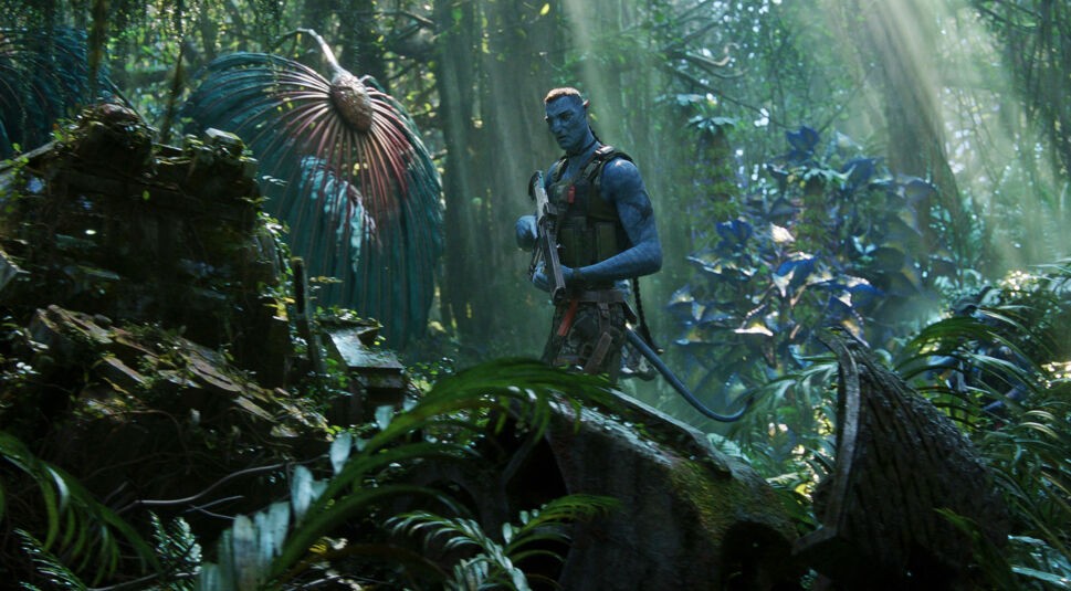 Auf dem Bild zu Avatar Fakten ist Colonel Quaritch, gespielt von Stephen Lang, in seiner Avatar-Form zu sehen. Er steht bewaffnet im üppigen, grünen Dschungel von Pandora, umgeben von exotischen Pflanzen und Lichtstrahlen, die durch die dichte Vegetation dringen. Seine ernste Miene und seine militärische Haltung betonen seine Entschlossenheit und Bedrohlichkeit.